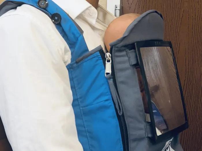A person wears a protype infant sling on the front of their body. The sling has a special window to allow light to reach the baby.